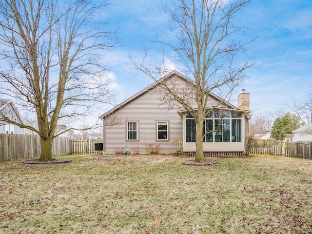 rear view of property featuring a sunroom, a fenced backyard, a chimney, and a lawn