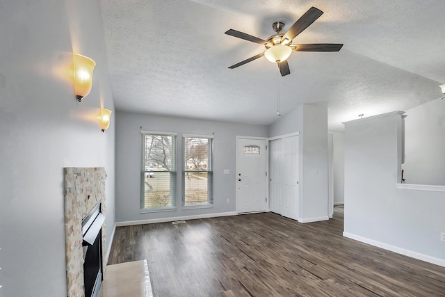 unfurnished living room with a fireplace, a textured ceiling, baseboards, and wood finished floors