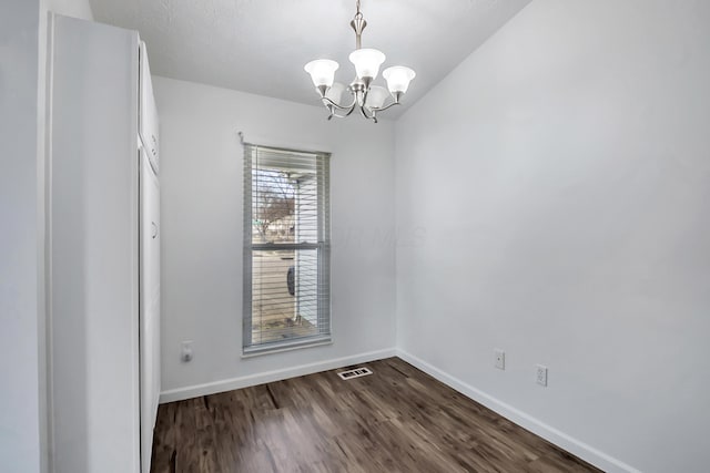 empty room featuring a chandelier, visible vents, baseboards, and dark wood-style floors