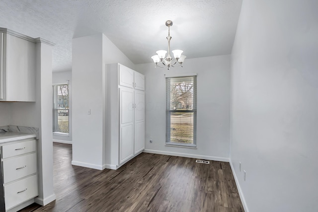 unfurnished dining area featuring a chandelier, a textured ceiling, visible vents, baseboards, and dark wood finished floors