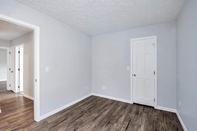 spare room featuring a textured ceiling, dark wood finished floors, and baseboards