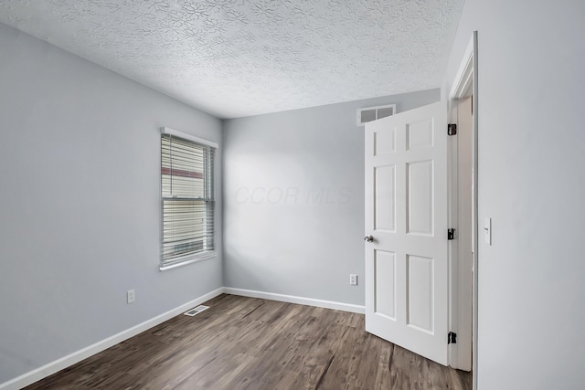 unfurnished room with a textured ceiling, wood finished floors, visible vents, and baseboards