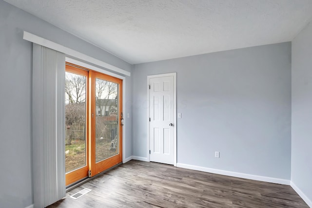 spare room with a textured ceiling, wood finished floors, visible vents, and baseboards