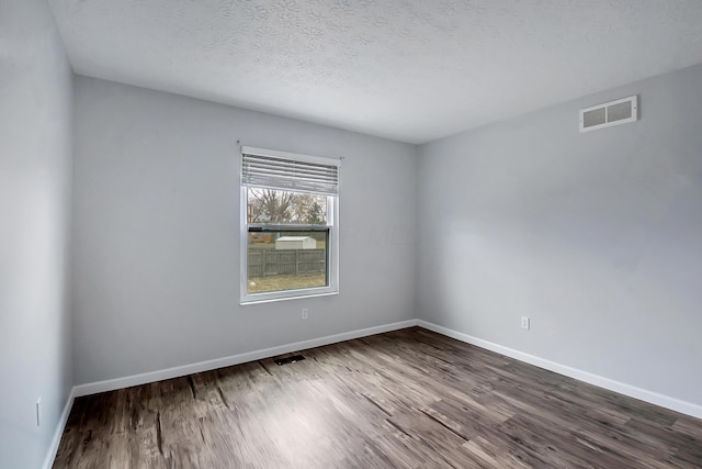 spare room featuring baseboards, a textured ceiling, visible vents, and wood finished floors