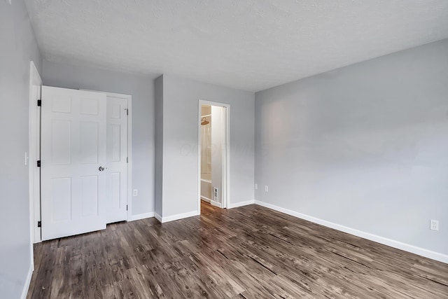 unfurnished bedroom featuring dark wood-type flooring, a textured ceiling, baseboards, and ensuite bathroom