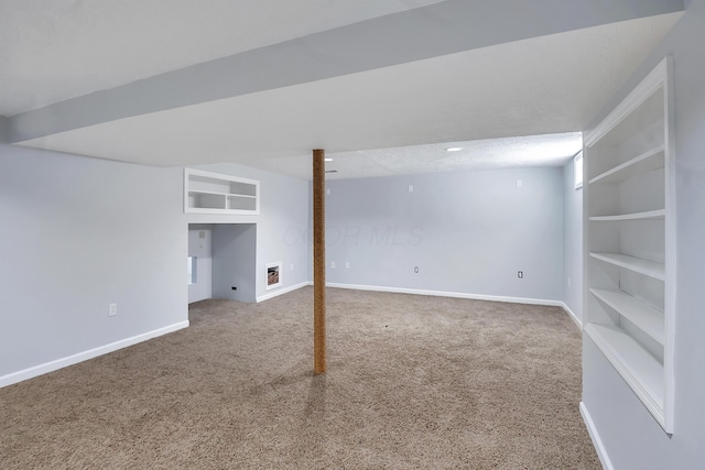 finished basement with carpet floors, built in shelves, a textured ceiling, and baseboards