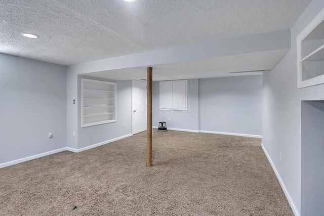 finished basement with built in shelves, carpet flooring, a textured ceiling, and baseboards