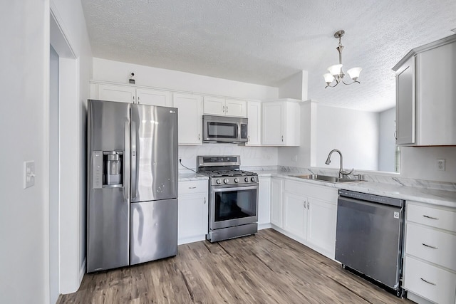 kitchen featuring stainless steel appliances, wood finished floors, a sink, light countertops, and decorative light fixtures