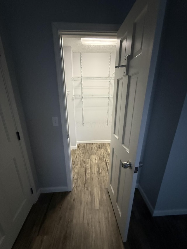 corridor featuring a textured ceiling, baseboards, and wood finished floors