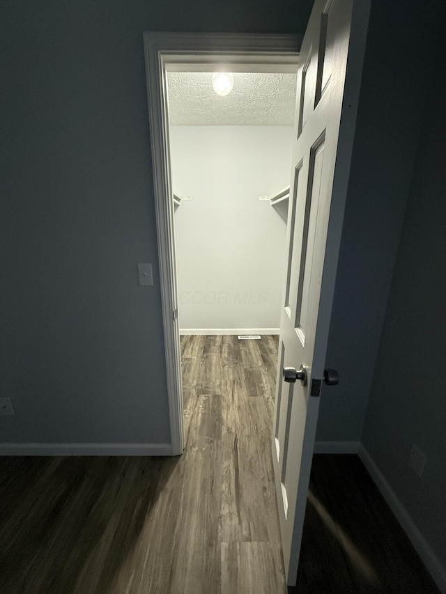 corridor with baseboards, a textured ceiling, and wood finished floors