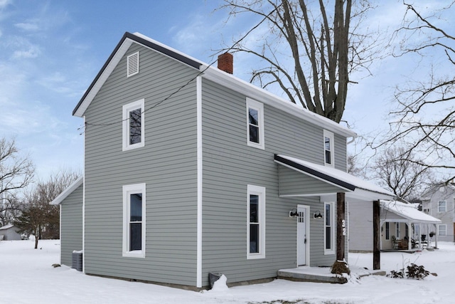 view of snowy exterior featuring central AC and a chimney