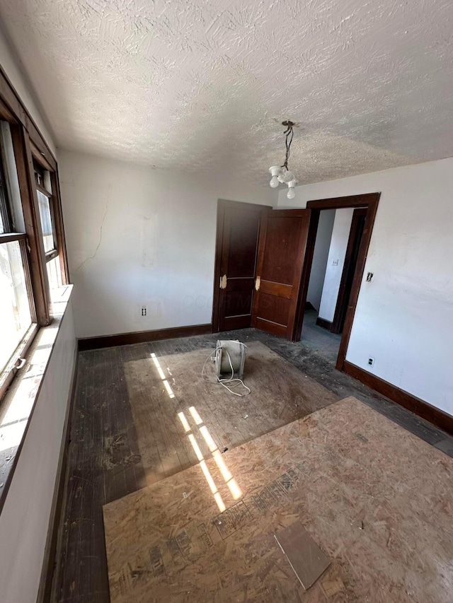 unfurnished room featuring wood-type flooring, a textured ceiling, baseboards, and an inviting chandelier