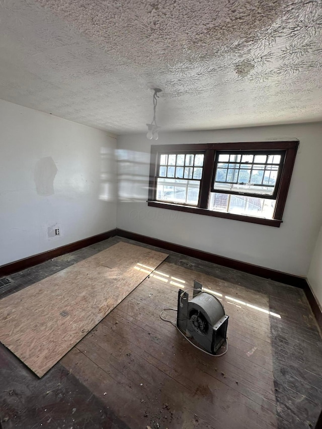 unfurnished room featuring a textured ceiling, plenty of natural light, hardwood / wood-style flooring, and baseboards