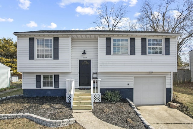 split foyer home with a garage, concrete driveway, and fence