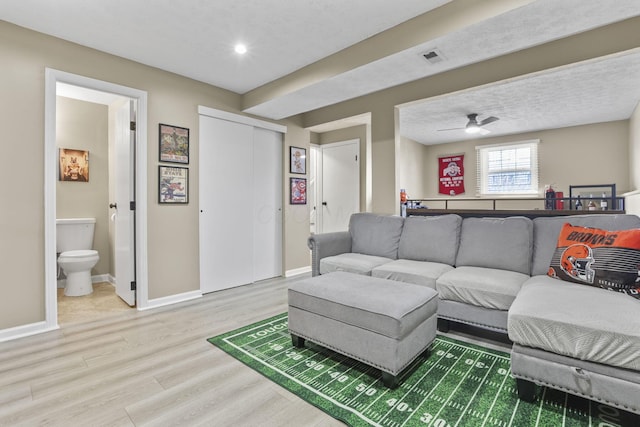 living room with a ceiling fan, visible vents, baseboards, and wood finished floors