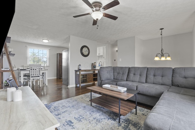 living room featuring ceiling fan with notable chandelier, a textured ceiling, baseboards, and wood finished floors