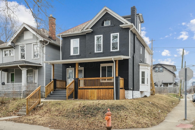 view of front of home with a chimney, a porch, and brick siding