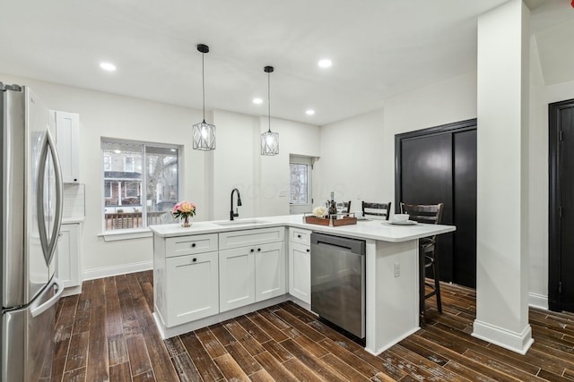 kitchen featuring dark wood finished floors, stainless steel appliances, light countertops, white cabinetry, and a sink