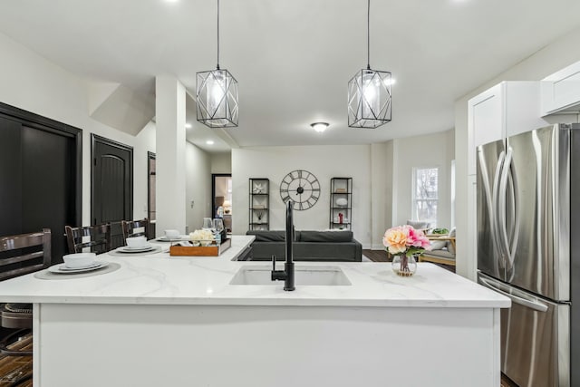 kitchen featuring light stone counters, pendant lighting, a center island with sink, freestanding refrigerator, and white cabinets