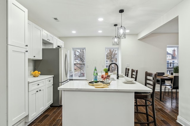 kitchen with a kitchen island with sink, white cabinetry, freestanding refrigerator, dark wood-style floors, and a kitchen bar