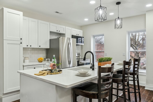 kitchen featuring dark wood finished floors, visible vents, decorative backsplash, appliances with stainless steel finishes, and a sink