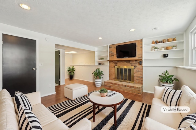 living area with built in features, visible vents, wood finished floors, a textured ceiling, and a brick fireplace