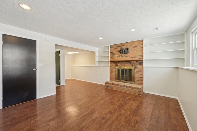 unfurnished living room featuring a fireplace, a textured ceiling, baseboards, and wood finished floors