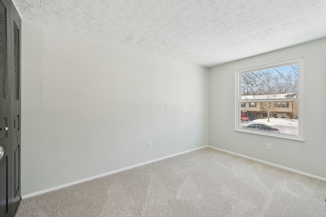 carpeted spare room with a textured ceiling and baseboards