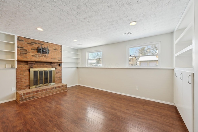 unfurnished living room featuring a fireplace, visible vents, a textured ceiling, wood finished floors, and baseboards