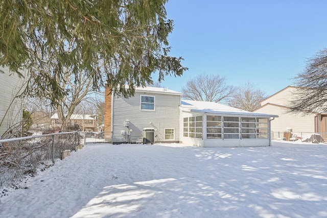 snow covered house featuring central AC unit, a sunroom, and fence