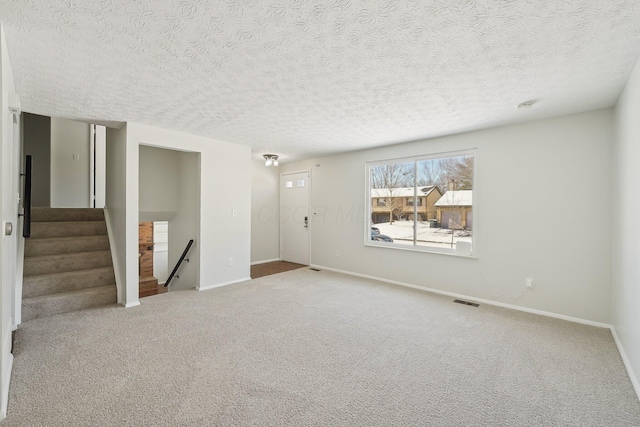 empty room featuring visible vents, baseboards, carpet, stairs, and a textured ceiling