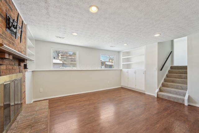 below grade area featuring visible vents, stairway, a brick fireplace, wood finished floors, and baseboards