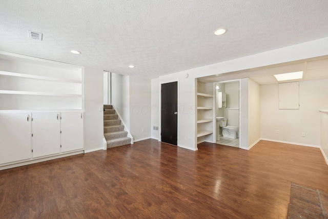 interior space with a textured ceiling, built in shelves, wood finished floors, baseboards, and stairway