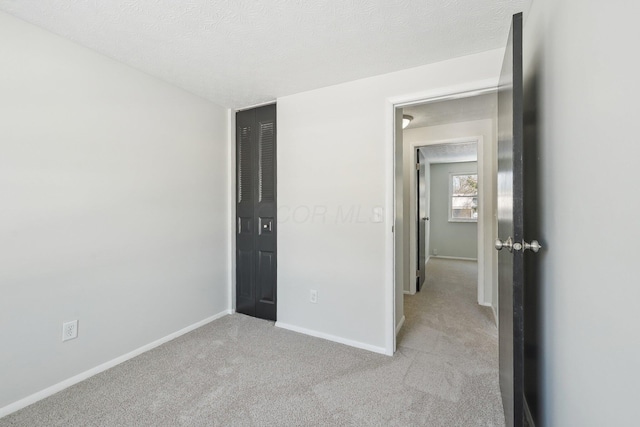 unfurnished bedroom featuring baseboards, a textured ceiling, and light colored carpet