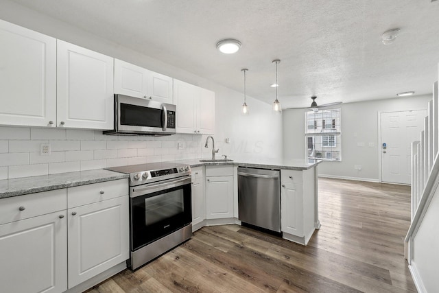 kitchen with a peninsula, a sink, stainless steel appliances, white cabinetry, and backsplash