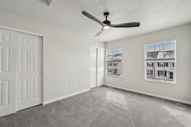 unfurnished bedroom featuring carpet floors, two closets, visible vents, a textured ceiling, and baseboards