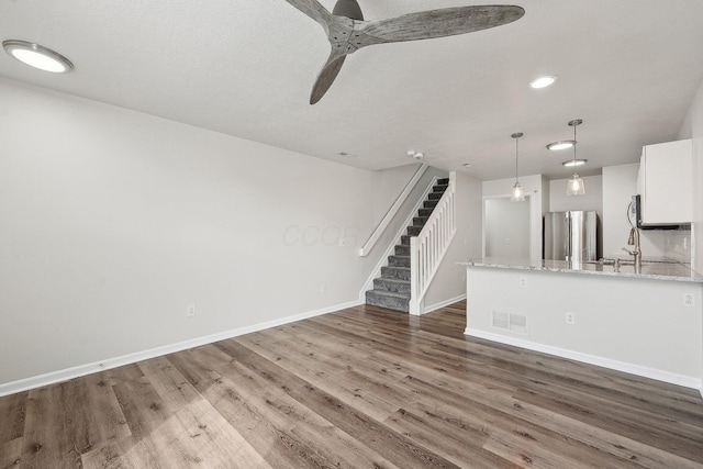 unfurnished living room with wood finished floors, visible vents, a ceiling fan, baseboards, and stairway