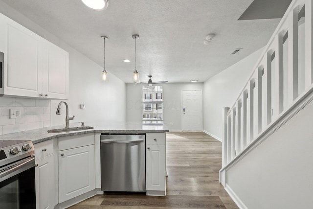 kitchen with stainless steel appliances, tasteful backsplash, a sink, wood finished floors, and a peninsula