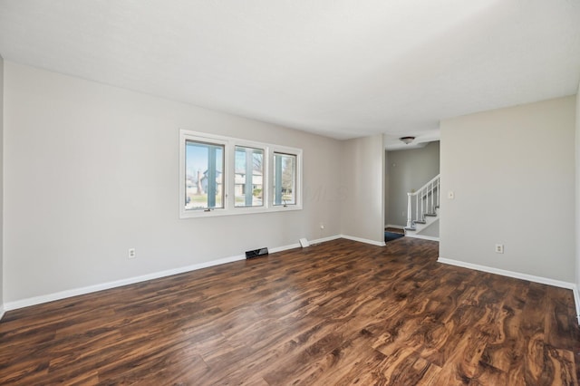 spare room with dark wood-type flooring, baseboards, and stairs