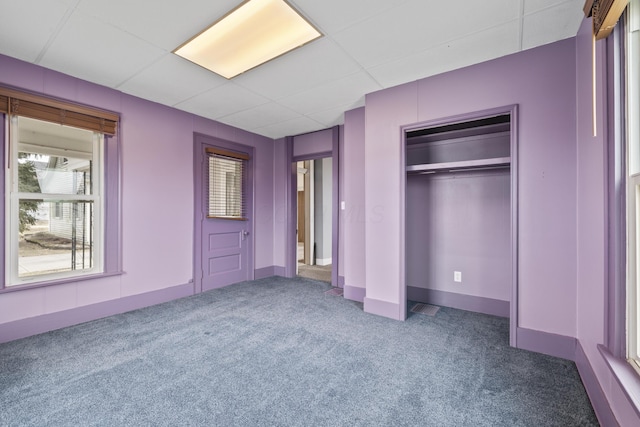 unfurnished bedroom with a paneled ceiling, a closet, baseboards, and carpet flooring