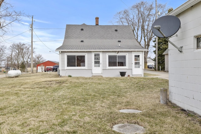 rear view of property with a yard, roof with shingles, and a chimney