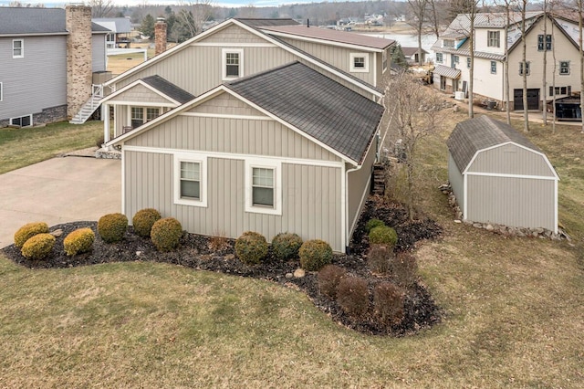 view of side of property featuring a residential view, roof with shingles, a storage unit, a yard, and an outdoor structure