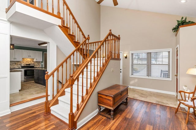 stairway with ceiling fan, a towering ceiling, baseboards, and wood finished floors