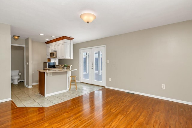 kitchen featuring baseboards, light wood-style floors, light countertops, french doors, and stainless steel microwave