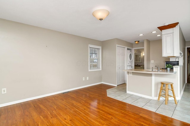 kitchen featuring a peninsula, a sink, baseboards, light wood-style floors, and a kitchen bar