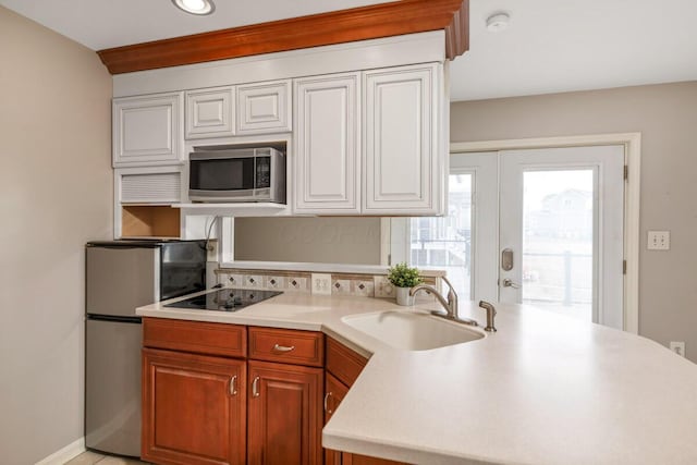 kitchen featuring decorative backsplash, appliances with stainless steel finishes, a peninsula, light countertops, and a sink