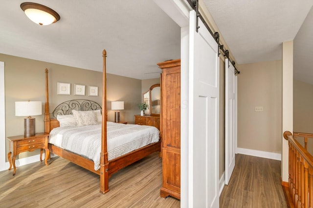 bedroom with light wood finished floors, a barn door, and baseboards