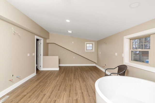 interior space featuring a freestanding tub, recessed lighting, wood finished floors, and baseboards