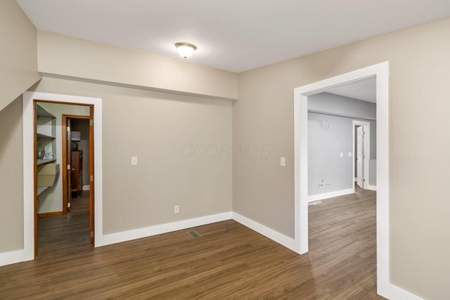 spare room featuring visible vents, baseboards, and dark wood-type flooring