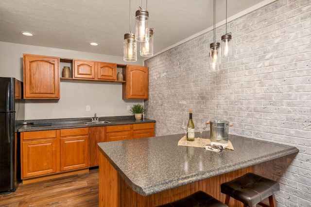 kitchen with dark wood-style floors, dark countertops, freestanding refrigerator, a sink, and a kitchen breakfast bar